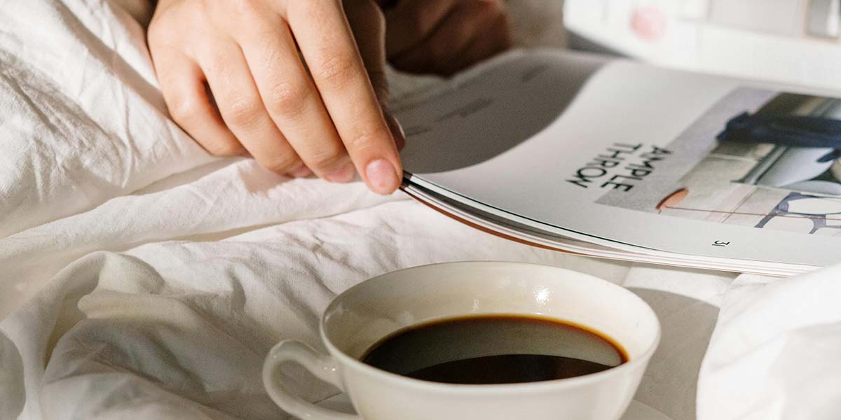 Person reading a magazine with coffee in bed